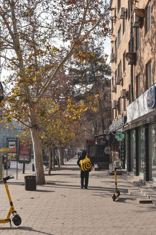Free A delivery person walks along a sunlit street in Yerevan, Armenia, showcasing daily urban life. Stock Photo