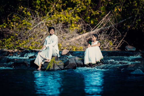Man and Woman in Traditional Clothing Sitting on the Rocks in a River 
