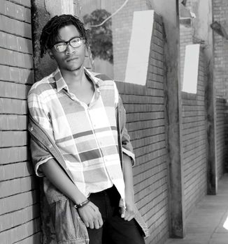 Stylish man in glasses poses casually against a brick wall, exuding modern fashion.