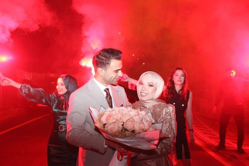 Free A joyful wedding couple holding flowers amidst red flares, embodying celebration and love. Stock Photo
