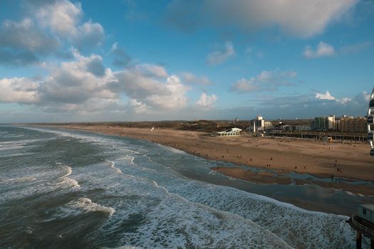 Drone shot of a sandy beach with gentle ocean waves and distant city skyline.