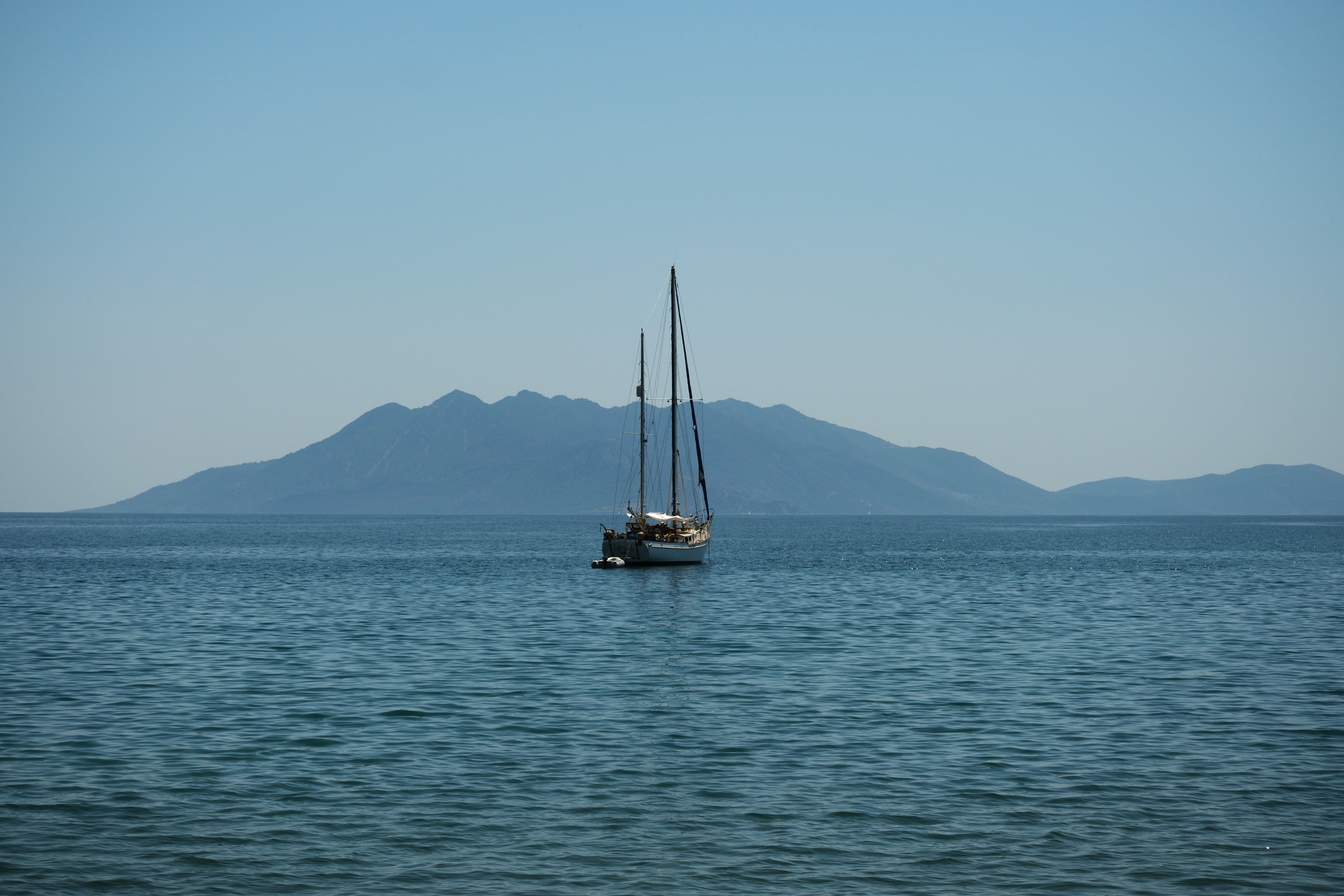 Incredible Milos: Small Group Yacht Tour—Kleftiko Sarakiniko Poliegos Review 2026 - A peaceful sailboat drifts near the island in Epidavros, Greece, under clear blue skies, creating a tranquil seascape.