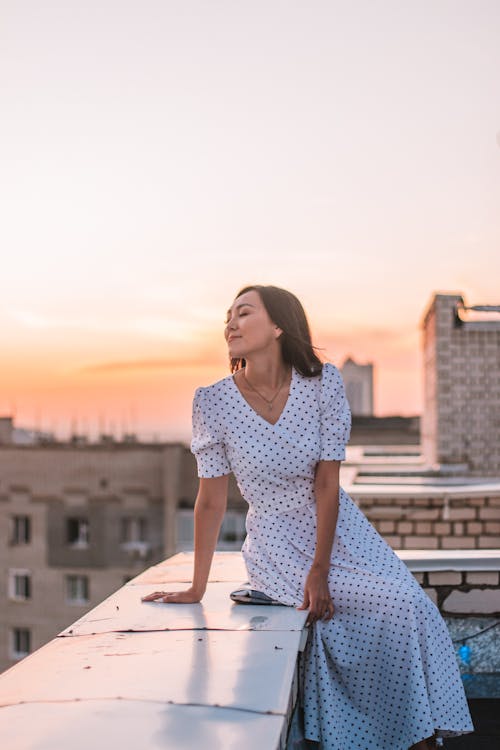 Young Woman in a Dress Sitting on a Rooftop Terrace at Sunset 