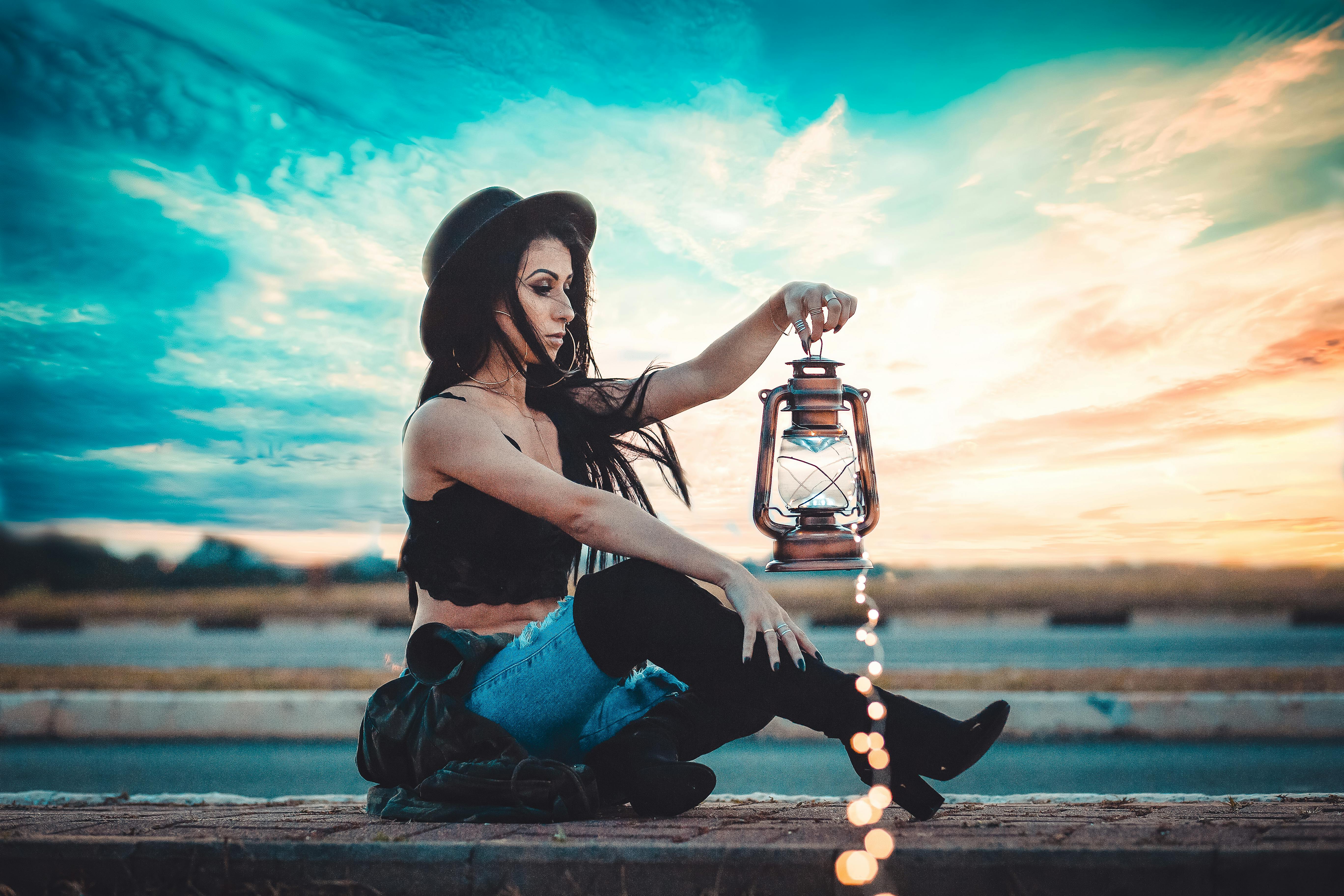 日落时分，一位戴着帽子的时尚女士手持灯笼，营造出梦幻般的氛围