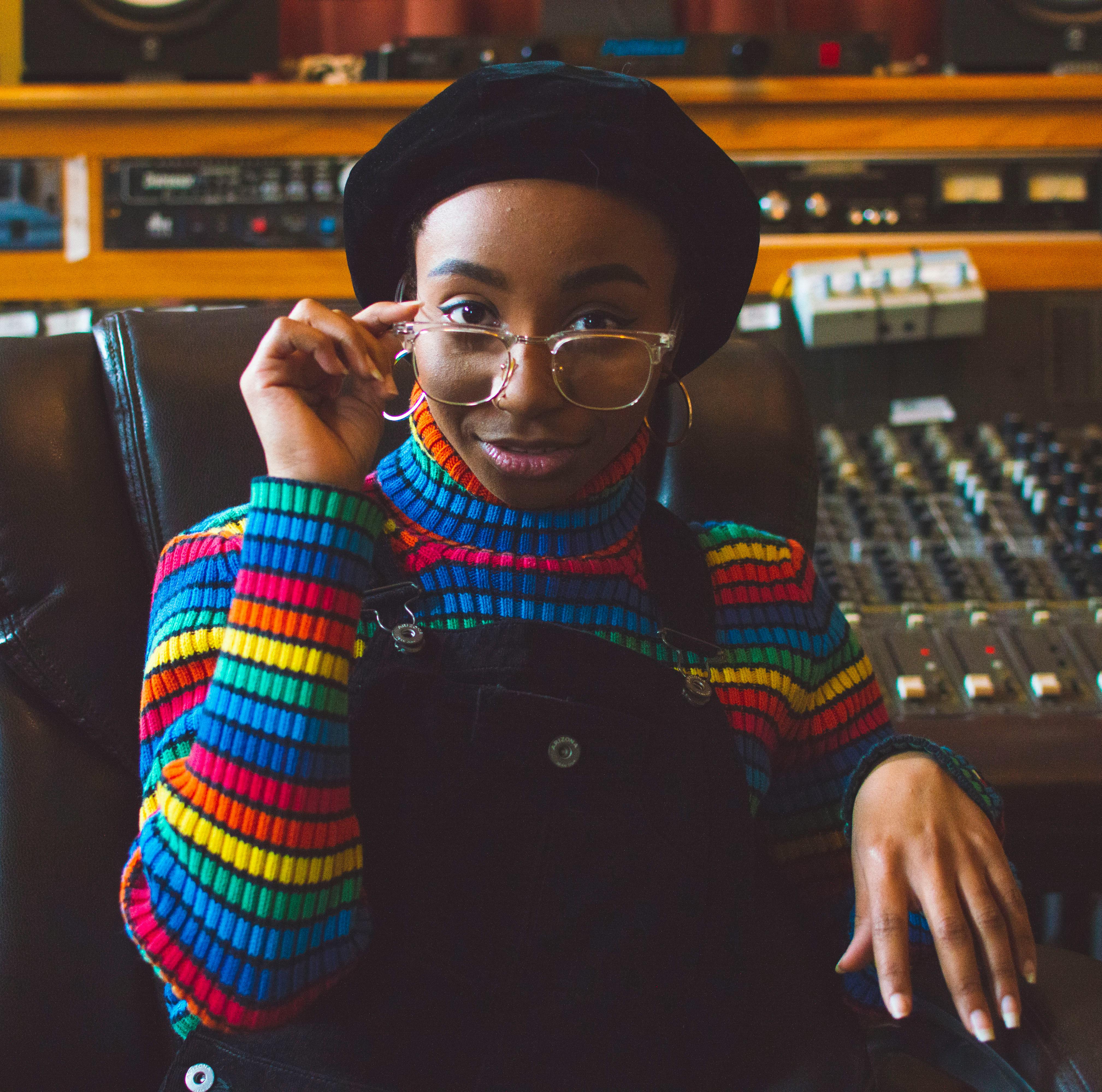 African American woman with eyeglasses in a colorful striped sweater sitting in a recording studio.