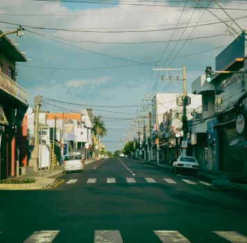 A quiet urban street lined with shops and parked cars, bathed in warm light.