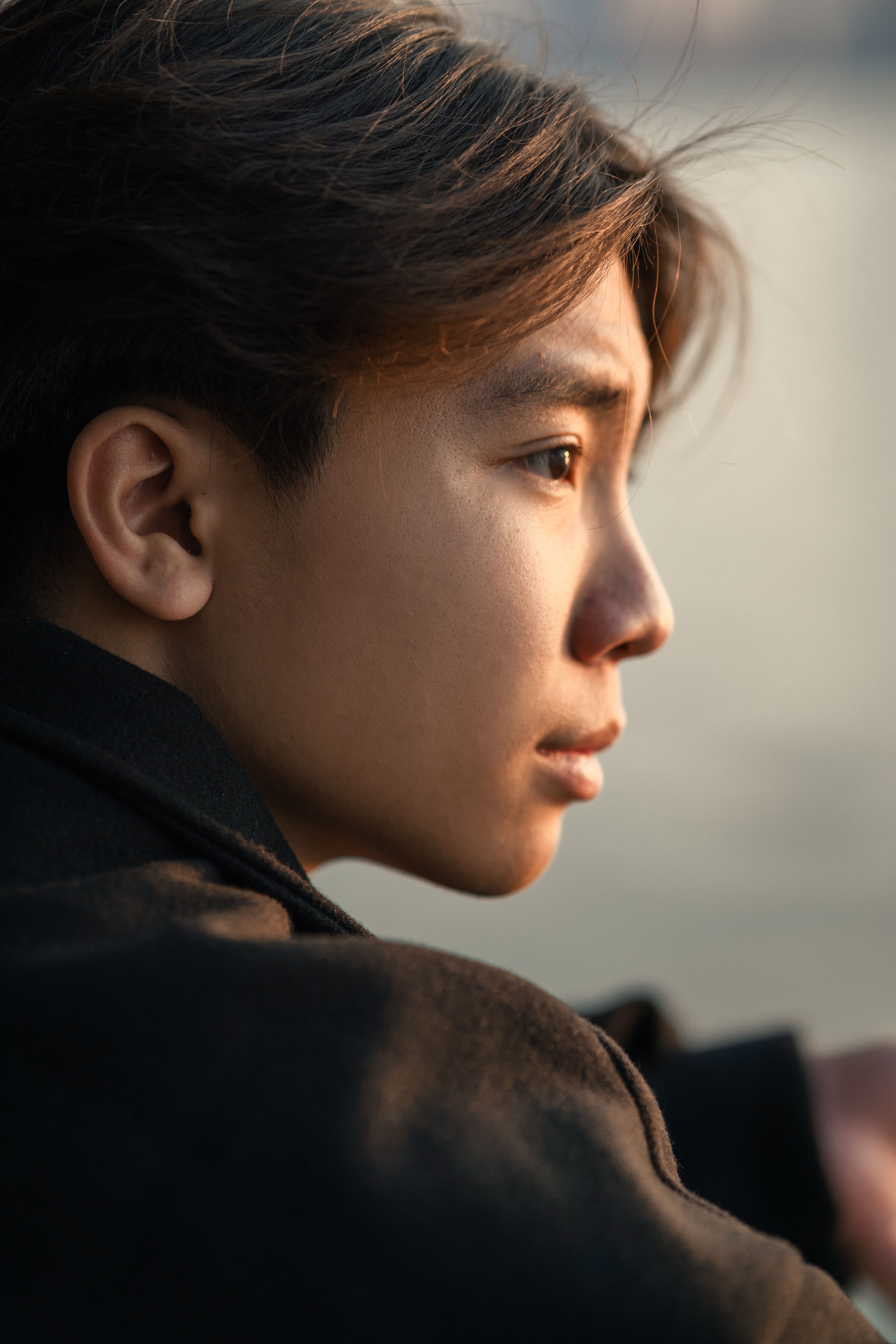 Profile shot of a young man outdoors in soft lighting, highlighting his contemplative gaze.