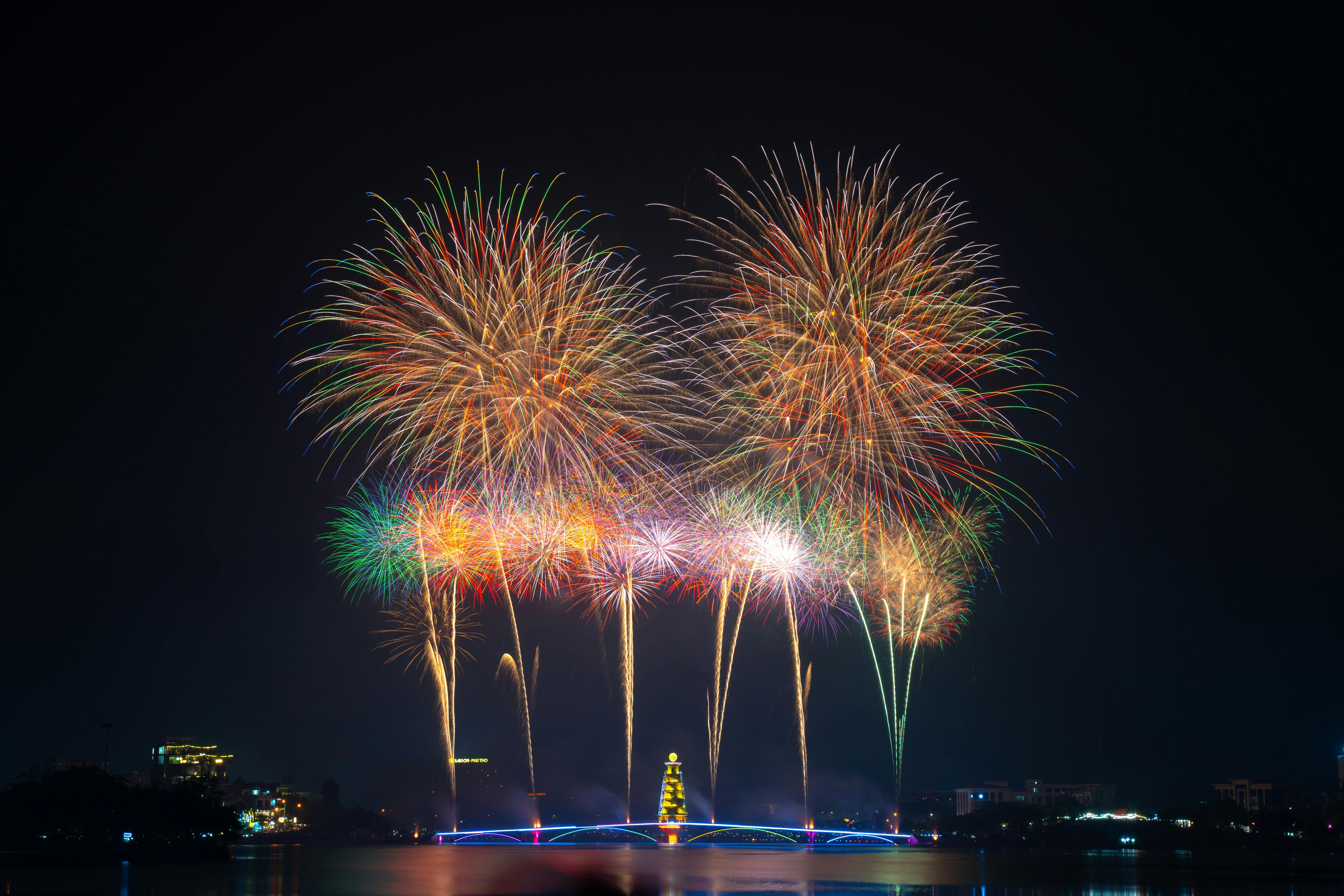Stunning multicolored fireworks exploding over water against a night sky, creating a vibrant celebra