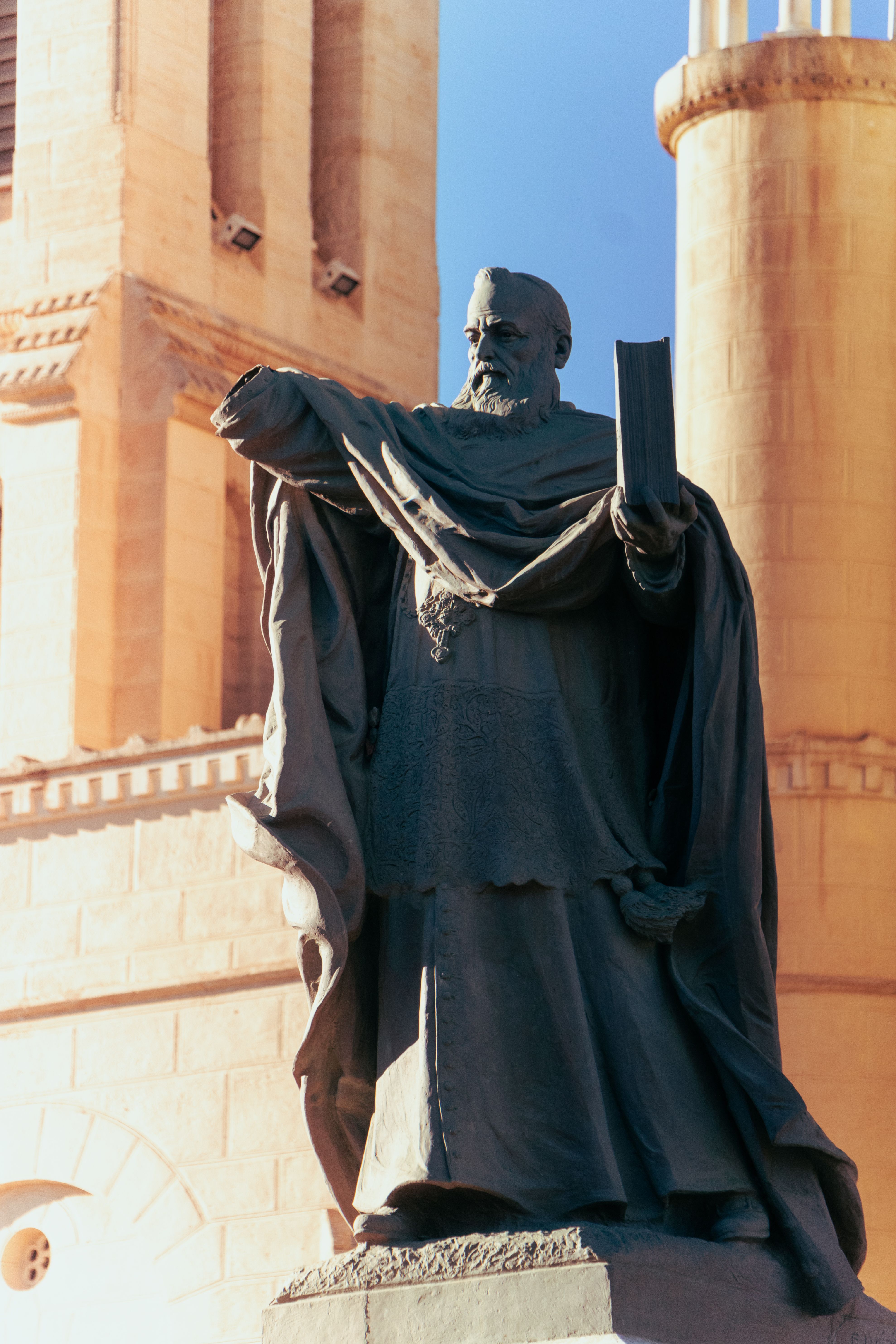 Monumental statue in front of cathedral showcasing historical religious figure with architectural background.