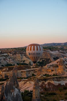 A hot air balloon floats over the rock formations of Cappadocia, Türkiye at sunrise, capturing breathtaking views.