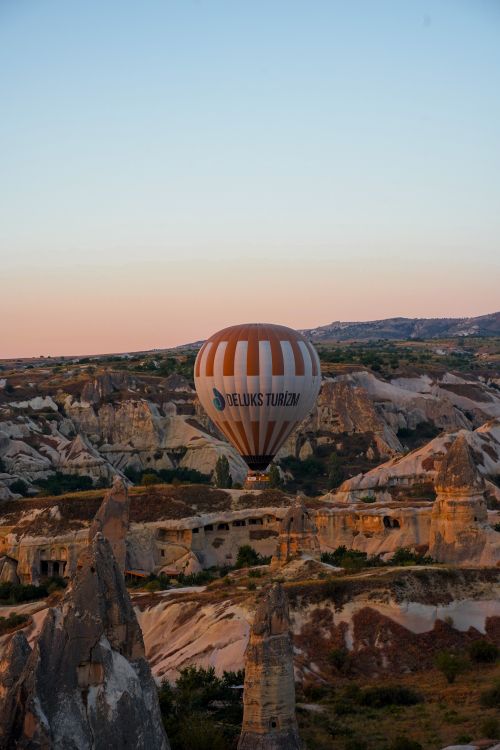 Free A hot air balloon floats over the rock formations of Cappadocia, Türkiye at sunrise, capturing breathtaking views. Stock Photo