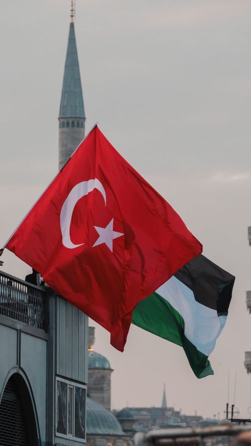 Free Turkish and Palestinian flags waving in the wind against an urban cityscape backdrop. Stock Photo