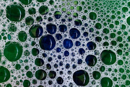 Close-up view of transparent water bubbles and soap foam on a base of colorful stones. Abstract background and wallpaper with green and blue tints	