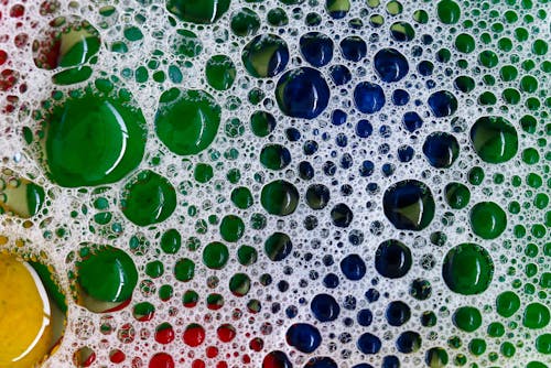 Close-up view of transparent water bubbles and soap foam on a base of colorful stones. Abstract background and wallpaper