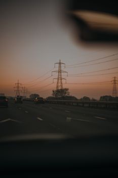 A serene view of cars driving under transmission towers during sunset in Chester, England.