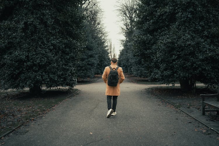 Man In Yellow Coat And A Backpack Walking Through A Park