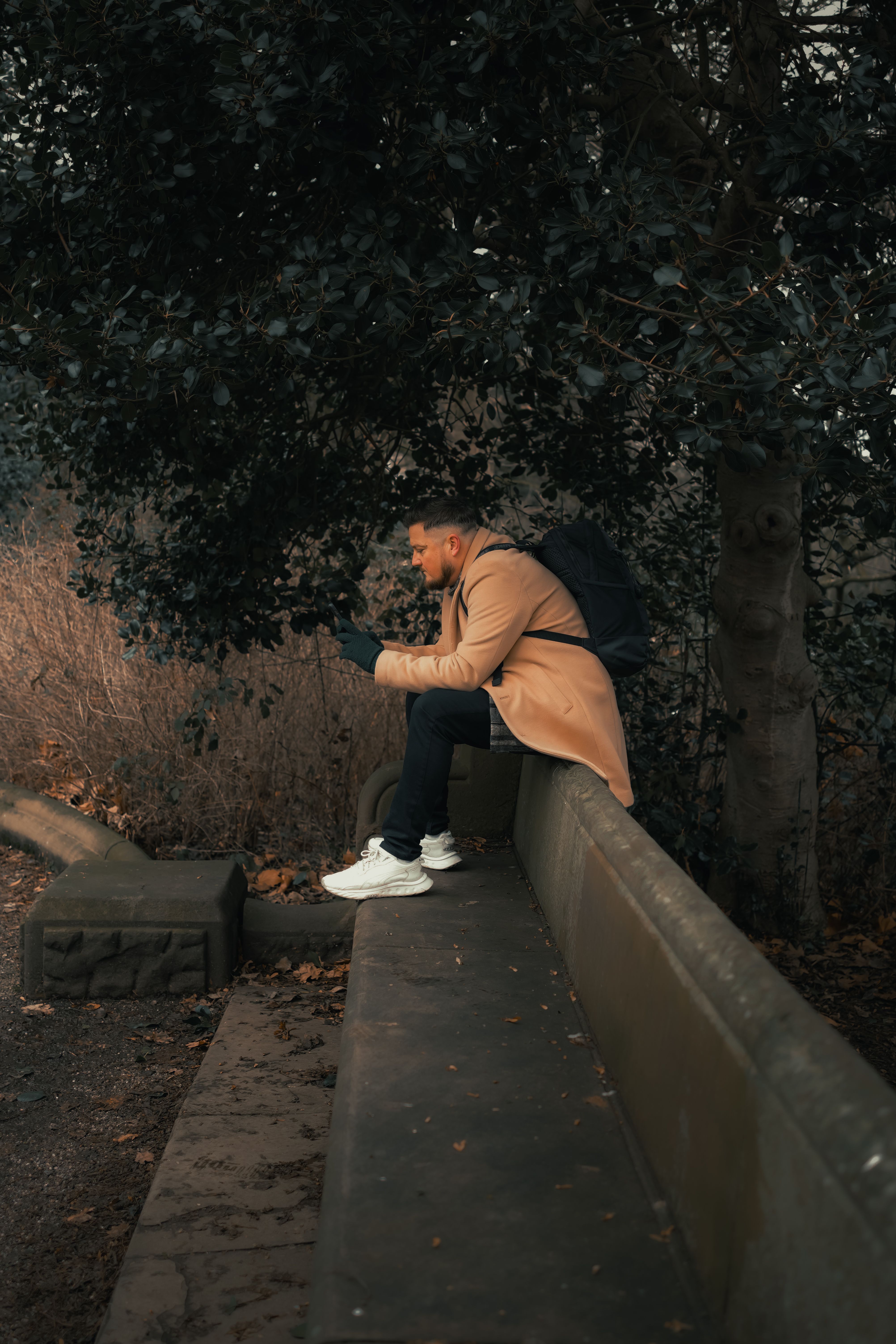 Man in a Brown Coat Sitting on the Back of a Concrete Bench in the Park ...