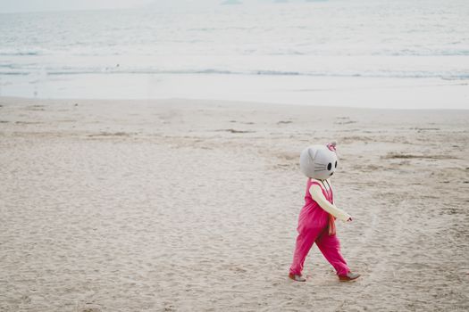 A child wearing a Hello Kitty costume strolls along a beach, with waves in the background.