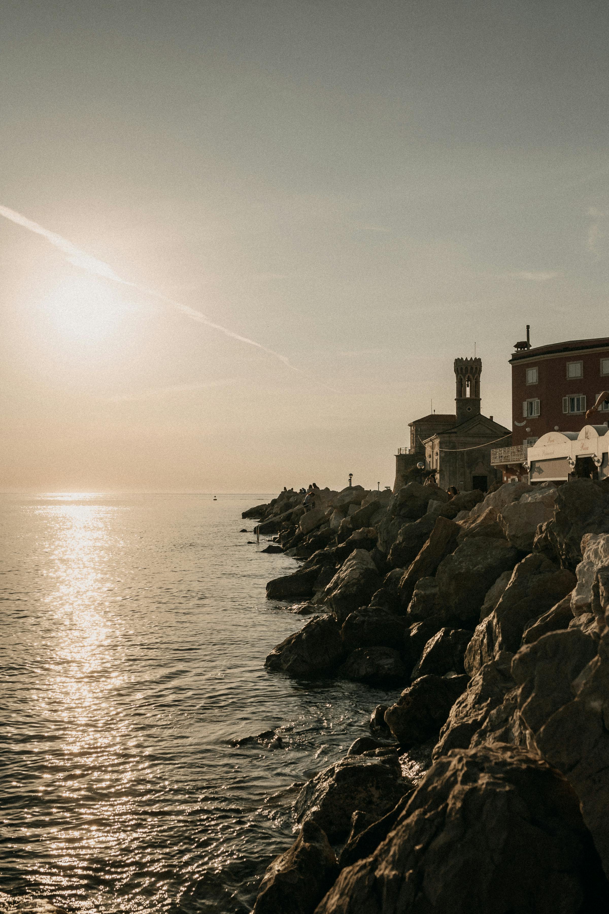 The sun sets over the rocky coastline of Piran, Slovenia, offering a serene and picturesque view.