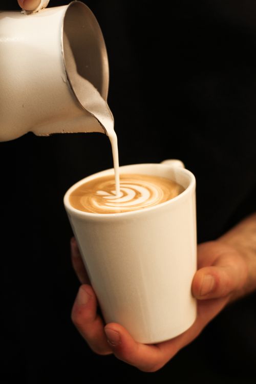 Free Artistic milk pour creating latte art in a cappuccino on a black background. Stock Photo