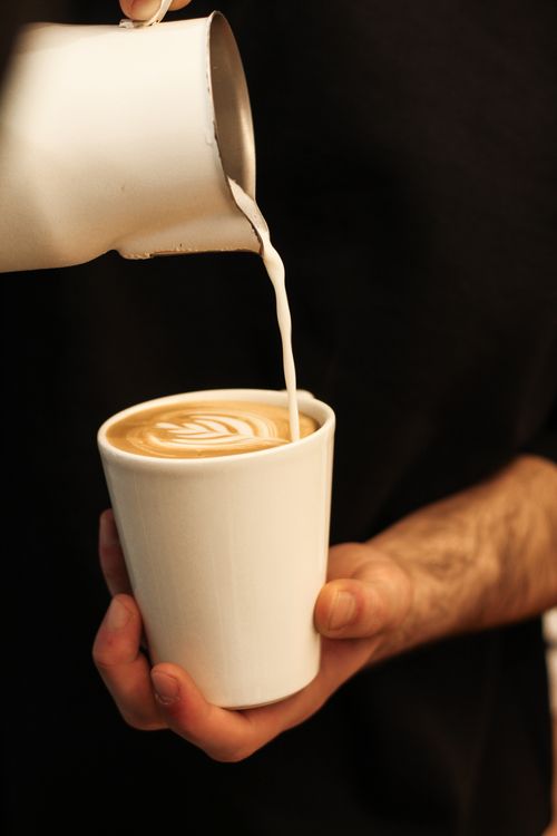 Free Barista skillfully pours milk to create froth art in a paper cup of coffee. Stock Photo
