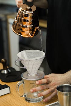 Close-up of hands preparing pour over coffee using a copper kettle and glass dripper.