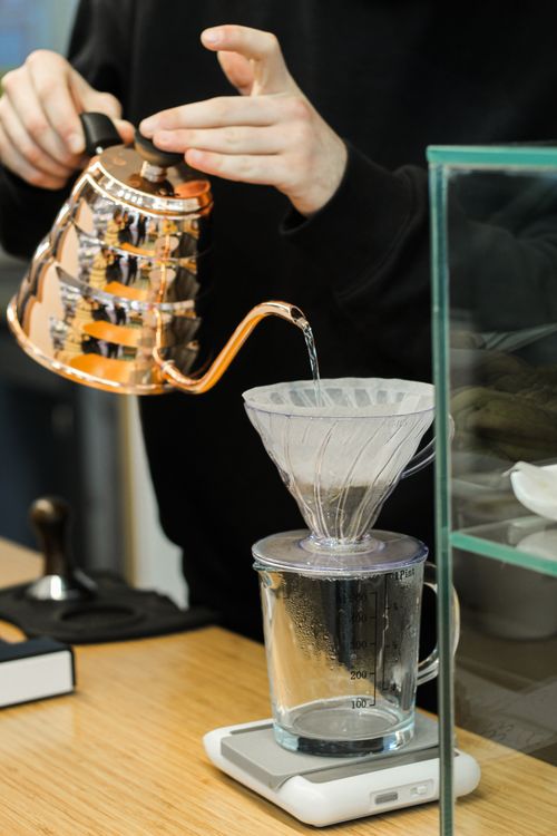 Free Close-up of a barista pouring hot water through a coffee dripper using a copper kettle. Stock Photo