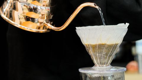 Close-up of hands pouring water in a pour-over coffee setup using a copper kettle.