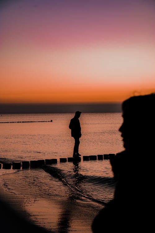 Silhouette of Man on Breakwater on Sea Shore at Sunset