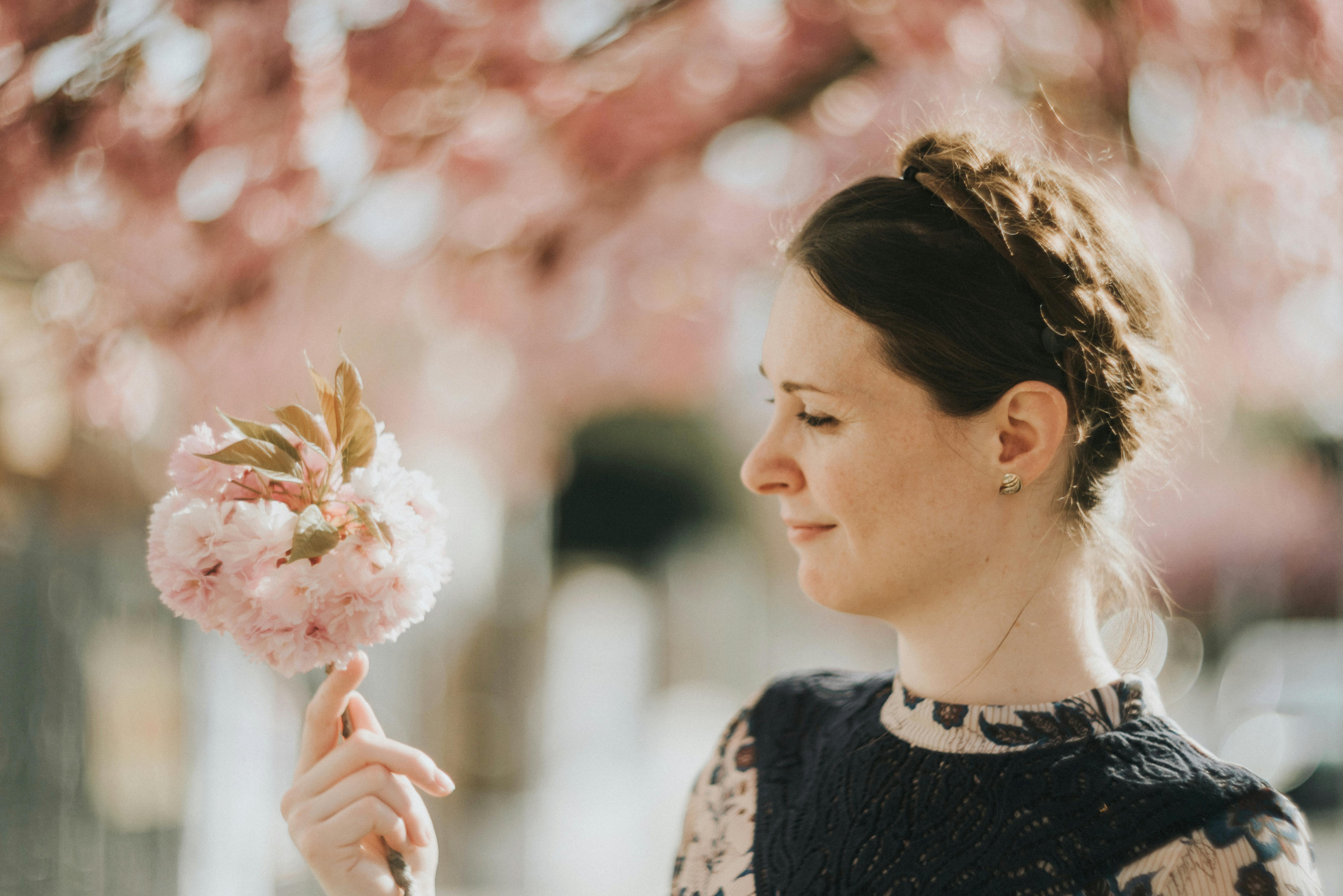 Portrait of a woman holding a pink flower bouquet outdoors during springtime.