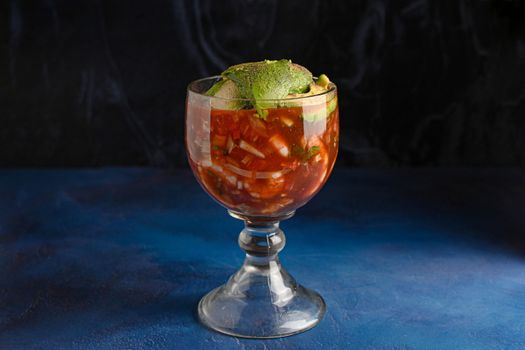 A refreshing glass of Mexican ceviche with avocado garnish on a dark background.