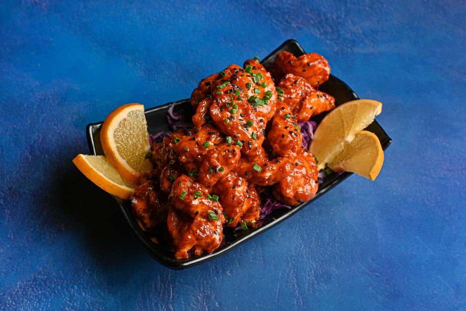 A plate of crispy golden fried shrimp coated in a creamy pink-orange bang bang sauce, garnished with sliced green onions.
