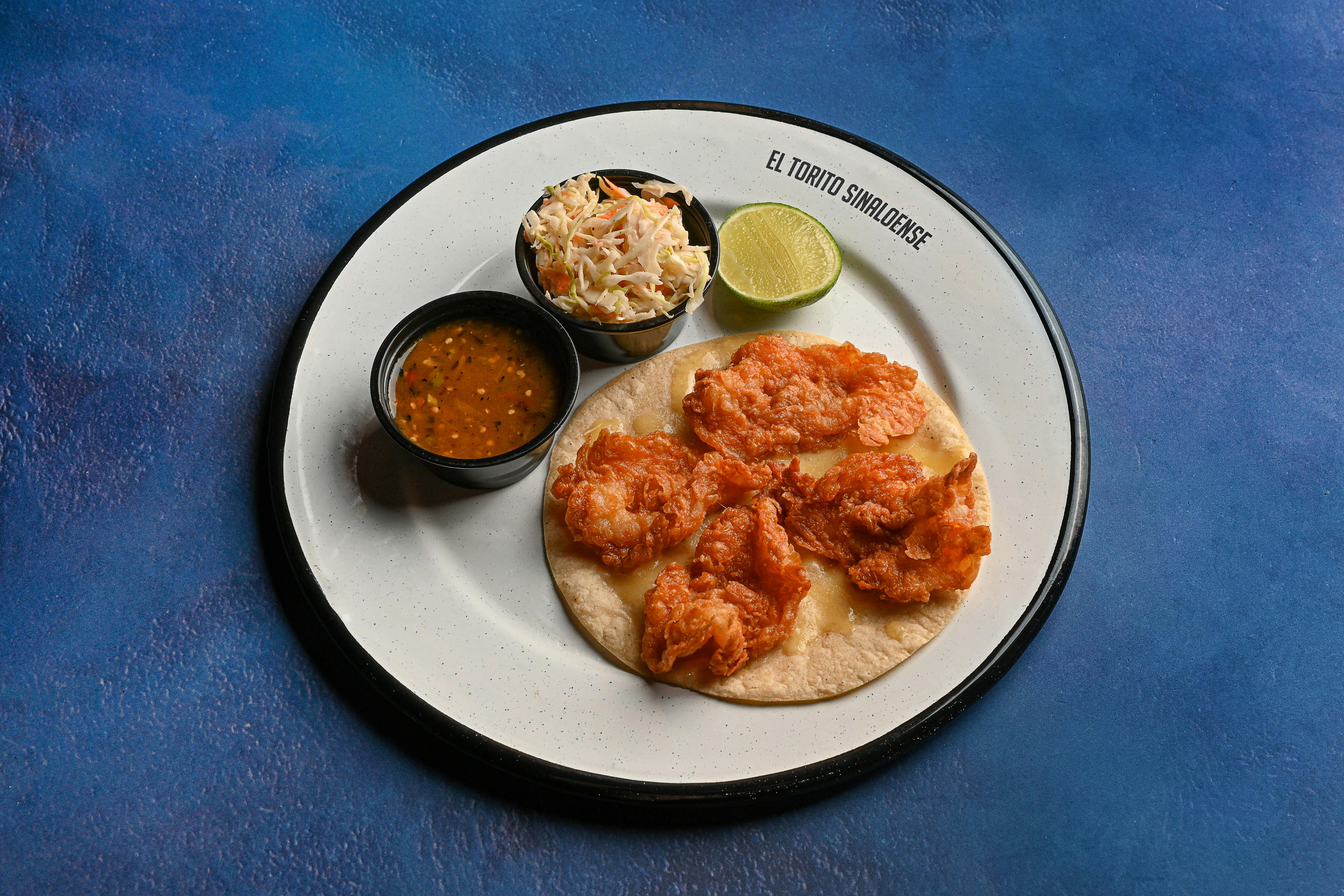 Crisp shrimp taco with coleslaw, salsa, and lime on a plate. Perfect food presentation.