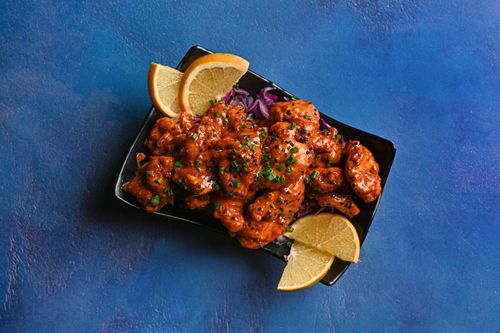 Free Tasty chicken dish garnished with lemon slices and fresh herbs on a vibrant blue backdrop. Stock Photo