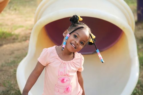 Free A joyful child with braids playing outdoors in a pink shirt and tube slide. Stock Photo