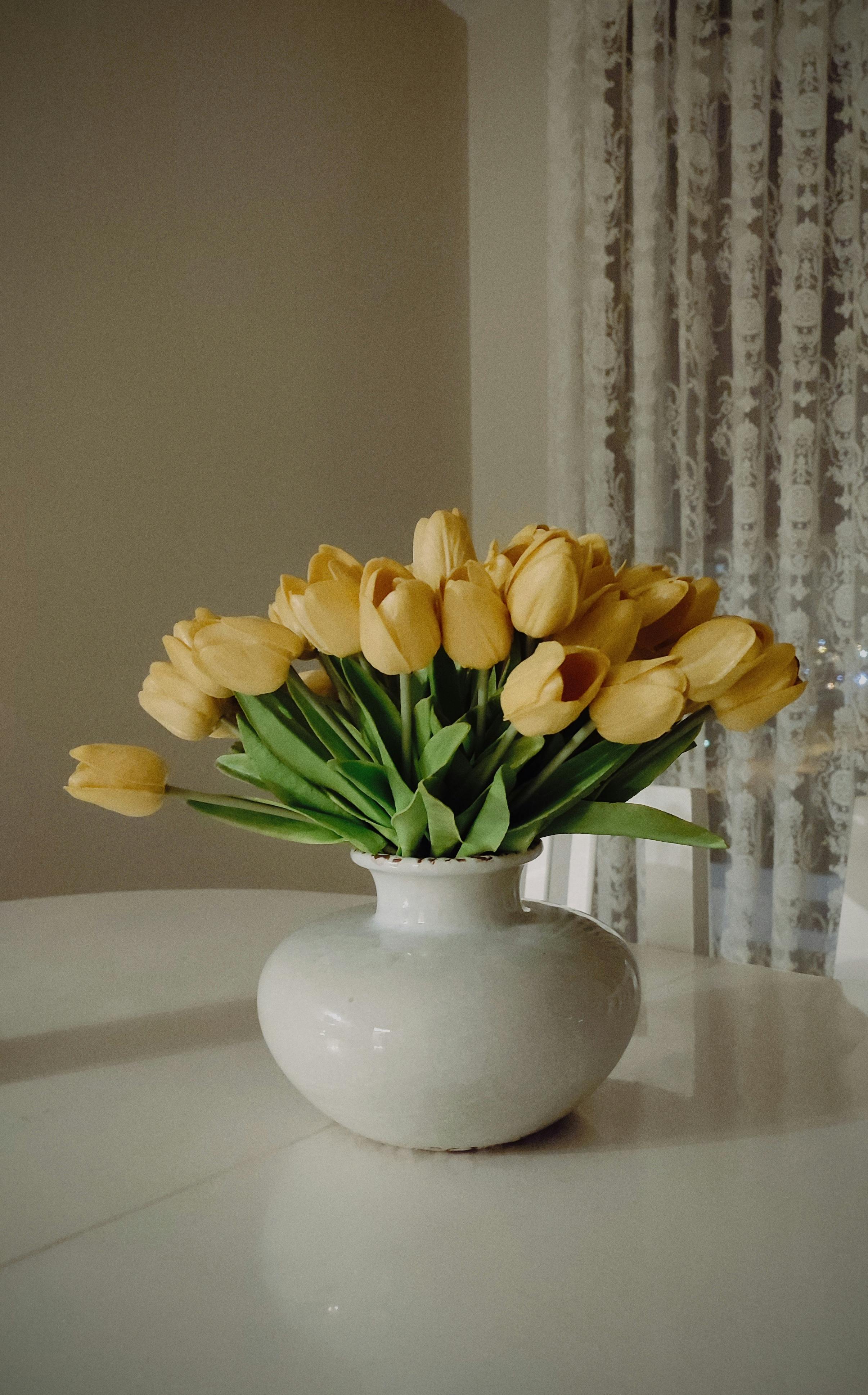 A beautiful bouquet of yellow tulips in a ceramic vase on a white table indoors.