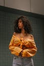 一位自信的女性身着休闲时尚的黄色上衣，留着卷发，正在室内摆姿势
