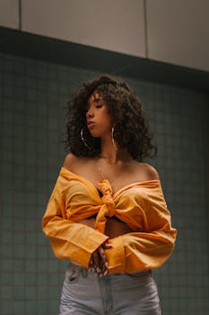 一位自信的女性身着休闲时尚的黄色上衣，留着卷发，正在室内摆姿势