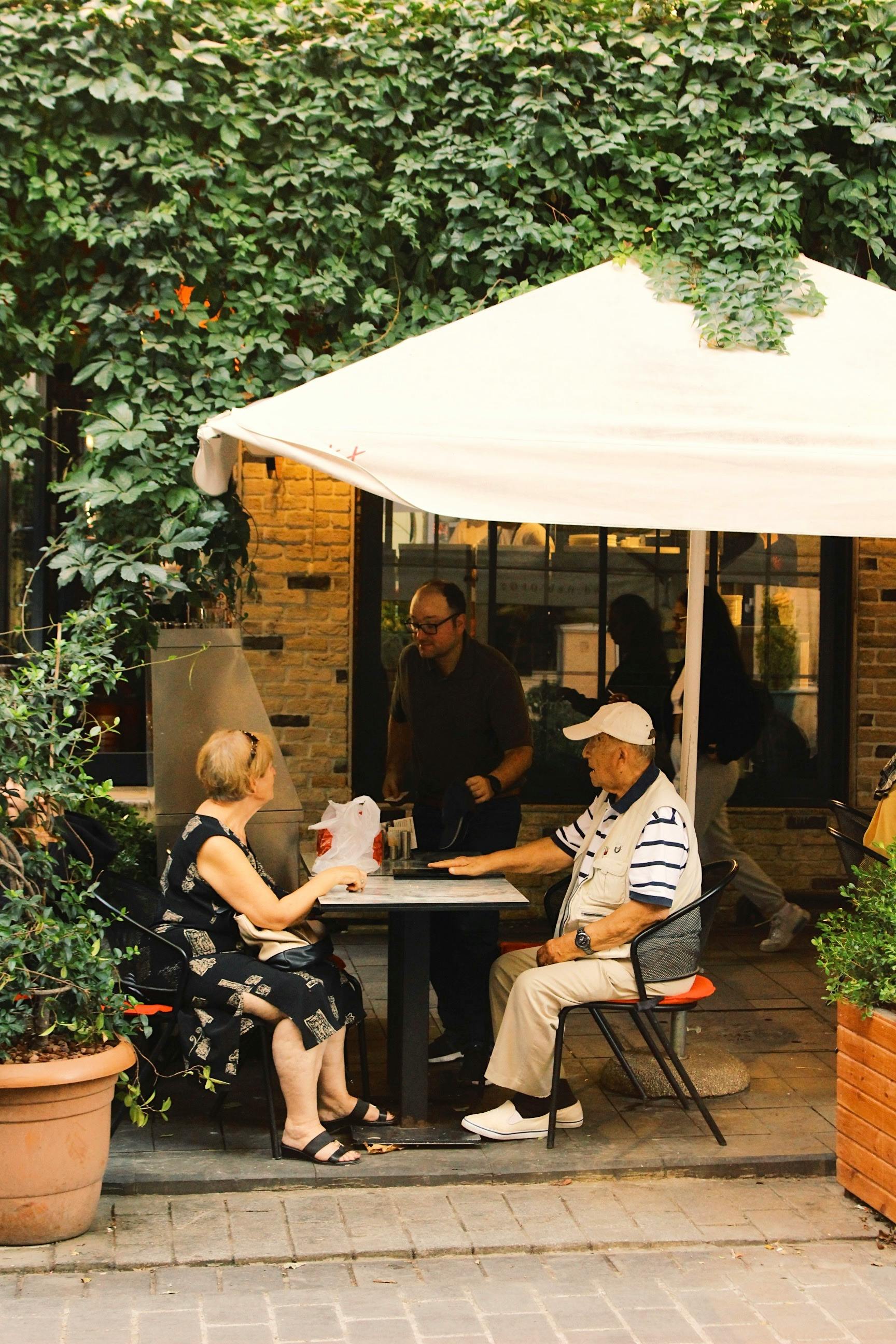 Elderly couple enjoys a meal at an outdoor café in Istanbul, Türkiye, under a large umbrella.