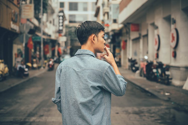 Young Asian Man Smoking Cigarette On Street