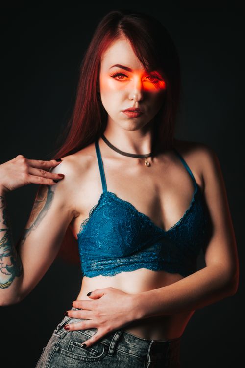 Free Studio portrait of a young woman with tattoos wearing a blue bra, showcasing a dramatic red light effect. Stock Photo