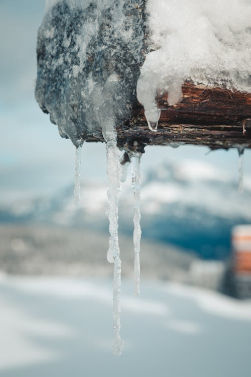 Icicles hanging from a wooden post with snow in the background