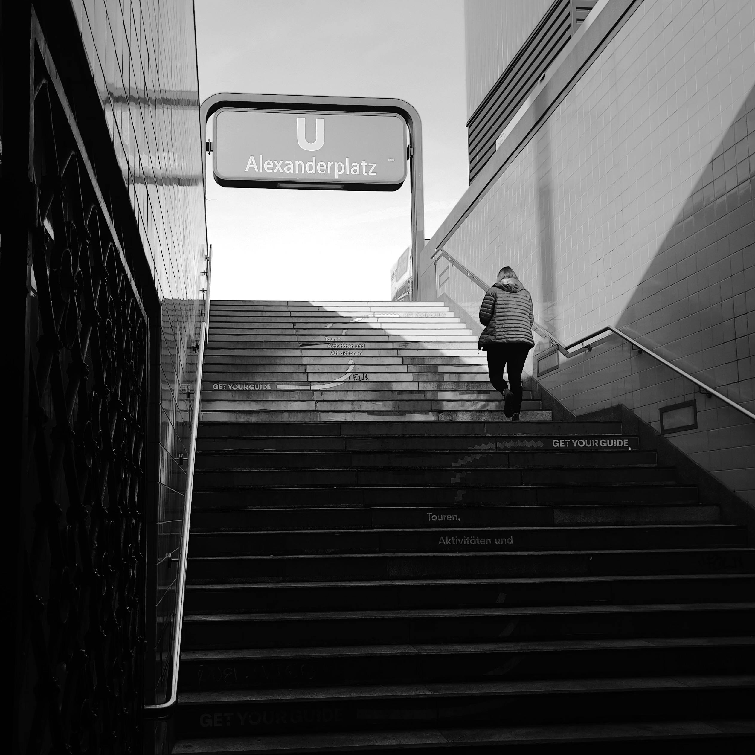 Monochrome view of a person ascending the stairs at Alexanderplatz metro station, Berlin.
