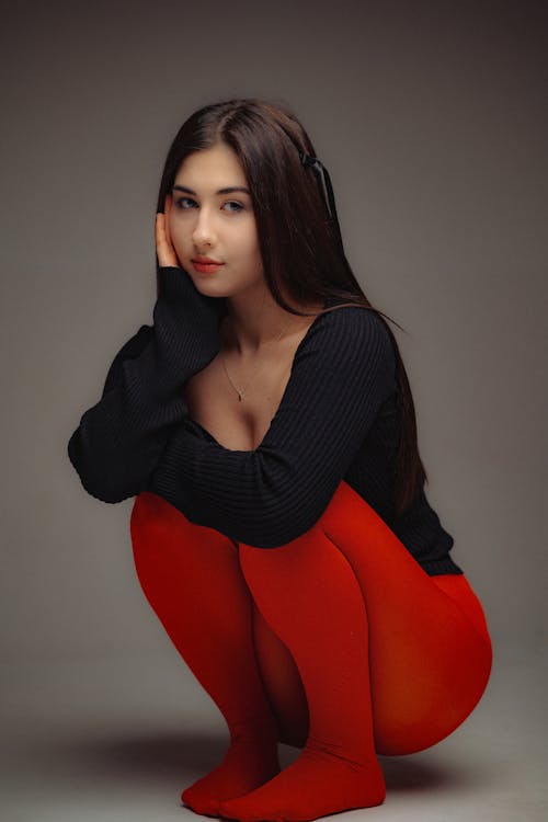 Foto profissional grátis de agachado, blusa preta, calças vermelhas