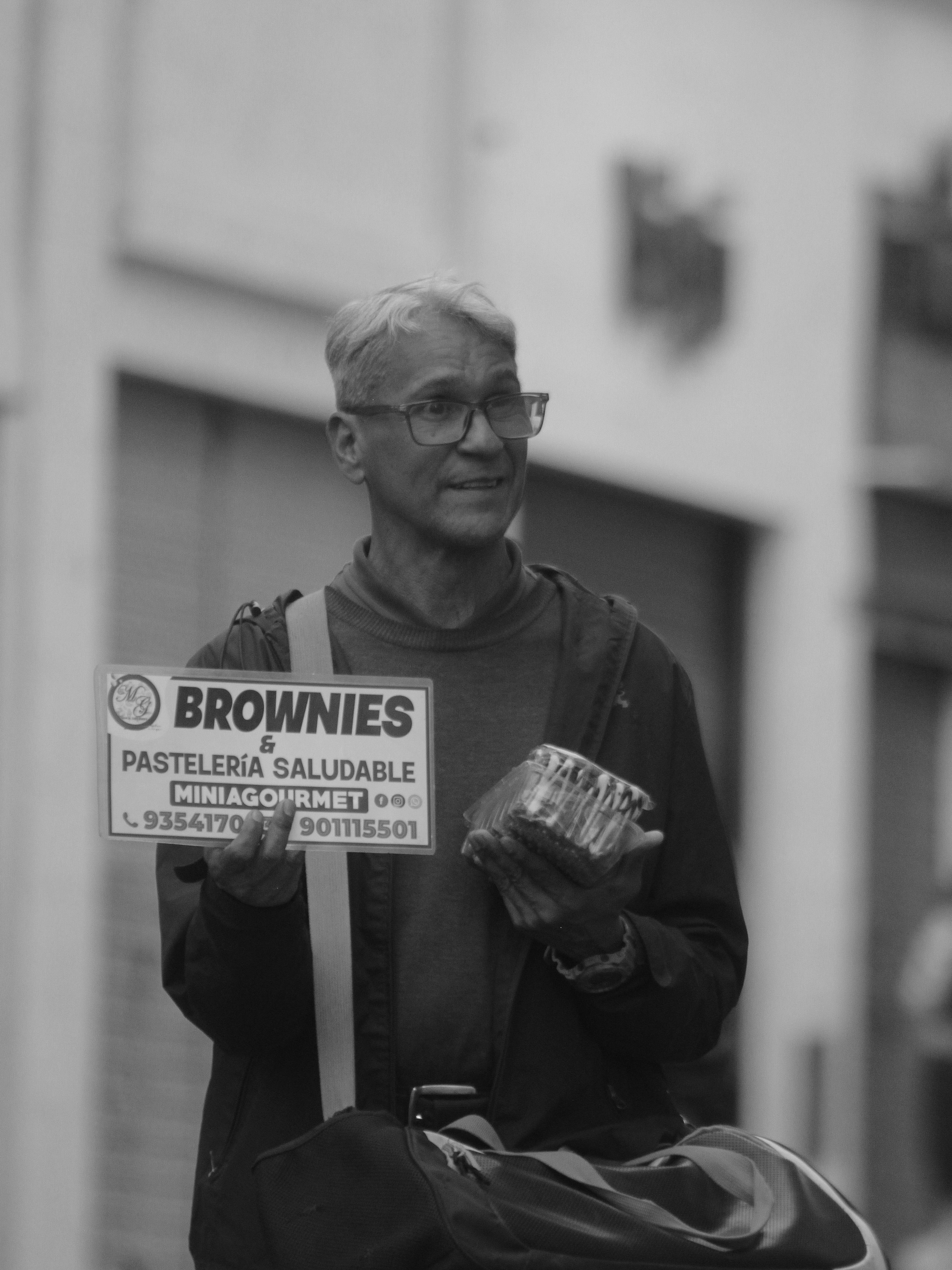 Black and white photo of an urban vendor holding brownies sign in the city streets.