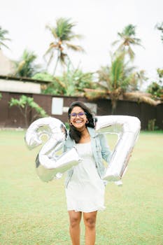 A cheerful woman celebrating her 27th birthday with balloons in an outdoor setting.