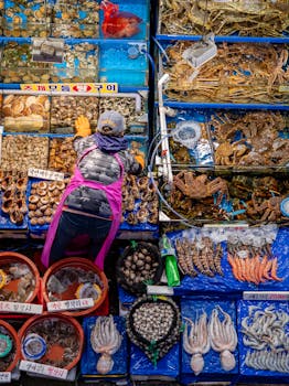 A bustling seafood market in Seoul, South Korea, showcasing a variety of fresh seafood and a vendor in action.