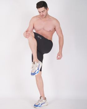 A shirtless man in sneakers posing during a studio fitness shoot.