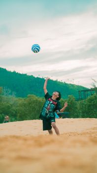 A boy enjoying a fun day playing volleyball on a sandy outdoor beach.