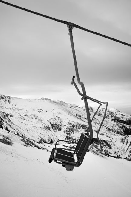 Black and white photograph of an empty ski lift over snow-covered mountains, capturing a serene winter landscape.